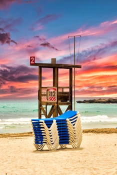 A lifeguard tower and a stack of sun loungers on the beach on the Mediterranean island of Mallorca with a beautiful colourful sunset