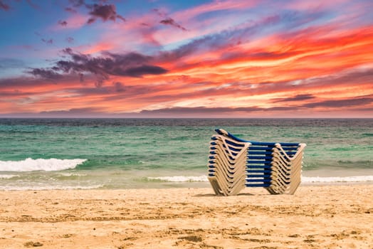 A stack of sun loungers stand on the beach on the Mediterranean island of Mallorca with a beautiful colourful sunset