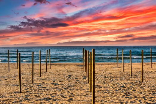 On the beach of Sa Coma on the Mediterranean island of Mallorca, wooden poles for the parasols are stuck in the sand with a beautiful sunset in the background