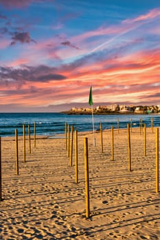 On the beach of Sa Coma on the Mediterranean island of Mallorca, wooden poles for the parasols are stuck in the sand with a beautiful sunset in the background
