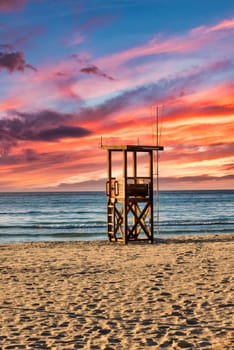 A lifeguard tower stands on the beach on the Mediterranean island of Mallorca with a beautiful colourful sunset
