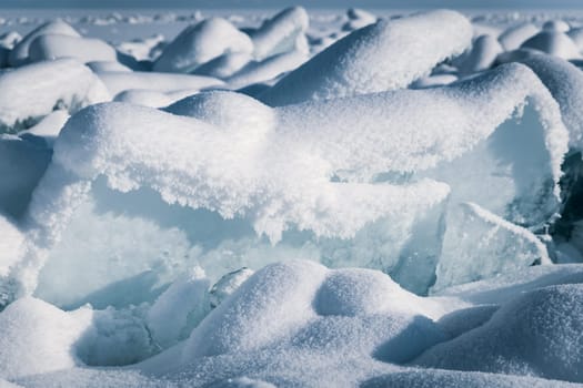 Transparent blue ice floes piled in ice hummocks against a blue sky on a sunny day. Unusual winter landscape of the frozen lake Baikal. Natural cold background. Siberia, Russia.