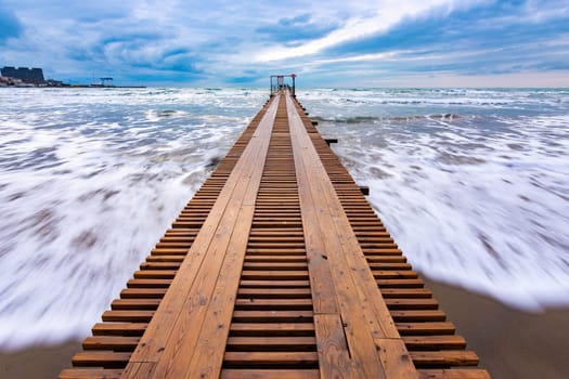Sea surf after sunset, a wooden pier goes into the distance