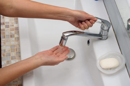 The girl opens the handle of the mixer in order to wash her hands