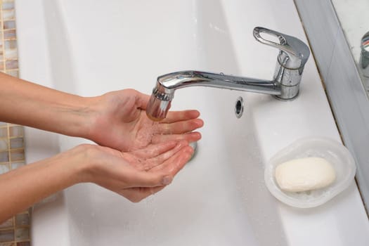 Girl pours water in the palm of the hand in the bathroom