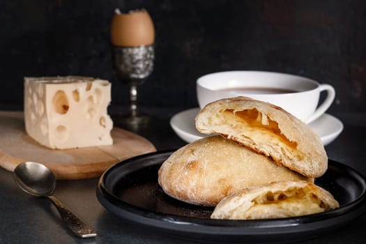 Cheese pie on a ceramic dish for breakfast with tea, a piece of cheese on a wooden board and an egg in a stand