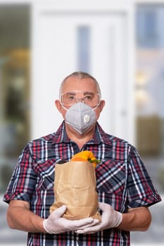 Coronavirus protective measures. Man with protective mask, safety goggles and medical gloves comes from a grocery store and carries a bag of fresh vegetables. Avoiding social contact and distance.