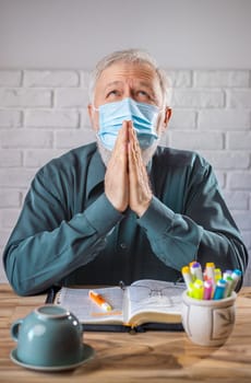 Man wearing medical mask on his face, before the Holy Bible and  a cup turned on his back, concept representing prayer and fasting for viruses protection