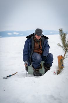 Baikal lake, Siberia, Russia - March 05, 2020 : Winter ice fishing. A fisherman is fishing on spinings near tents and cars on Lake Baikal on a March day. Baikal lake, Siberia, Russia