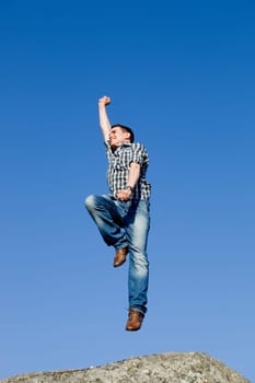 young happy man, with a big jump, on top of a rock
