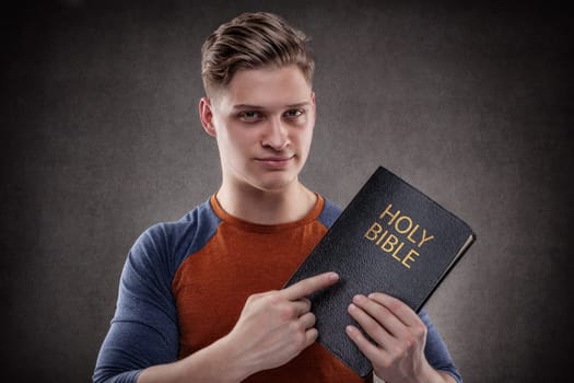 Happy young man pointing his Holy Bible with leather covers