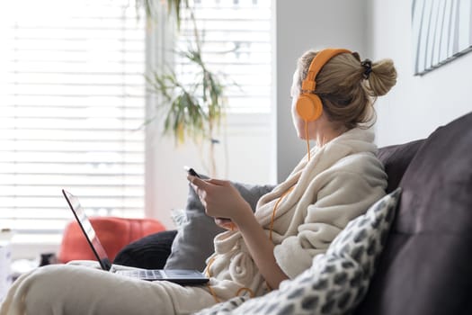 Woman in bathrobe being comfortable at her home sofa, using social media apps on phone for video chatting and stying connected with her loved ones. Social distancing. Stay at home.