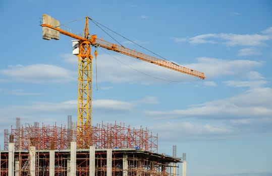 Construction site background. Yellow tower crane and building under construction against blue sky. Industry concept.