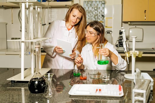 Two female laboratory technicians researching medical samples and reagents for coronavirus or covid 19 vaccination and uploading data through tablet