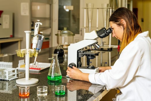 Female doctor or lab technician checking or researching covid 19 virus samples under microscope to help with discovery of coronavirus vaccination