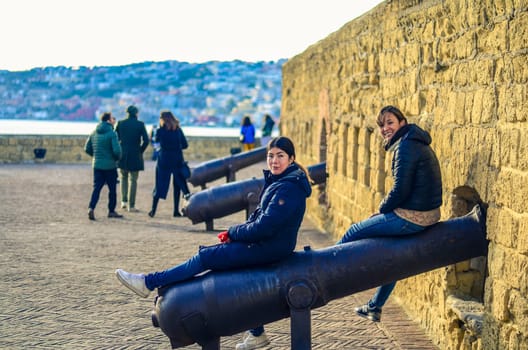 two women sit on the old guns and fortifications in the Castel dell'Ovo (Egg Castle) in Naples, Italy