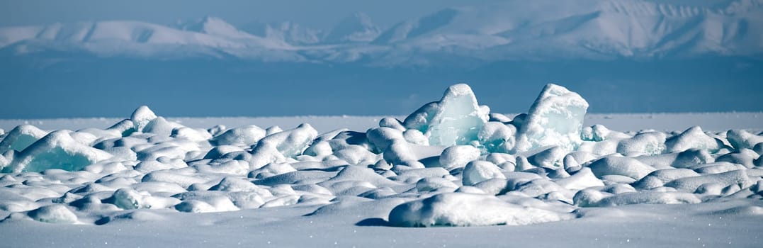 Transparent blue ice floes piled in ice hummocks against a blue sky on a sunny day. Unusual winter landscape of the frozen lake Baikal. Natural cold background. Siberia, Russia.