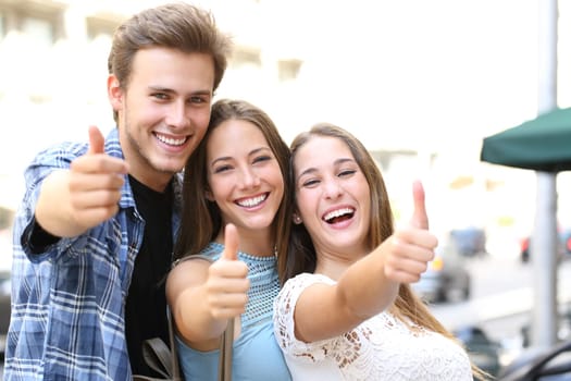 Happy group of three friends with thumbs up and perfect smiles looking camera in the street