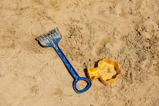Children's toys, shovel and sand mold lie on light sand