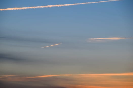 Contrail from an airplane on a blue sky against a sunset.