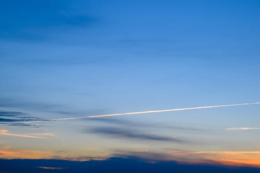 Contrail from an airplane on a blue sky against a sunset.