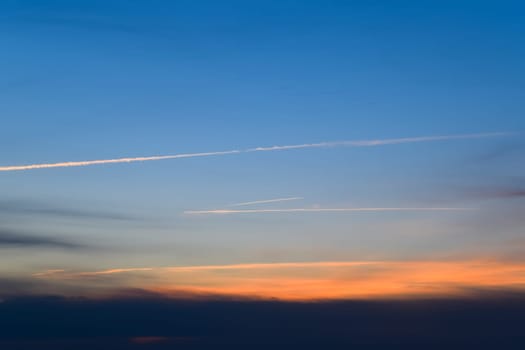 Contrail from an airplane on a blue sky against a sunset.