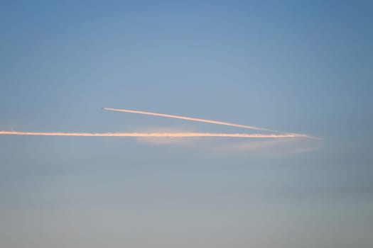 Contrail from an airplane on a blue sky against a sunset.