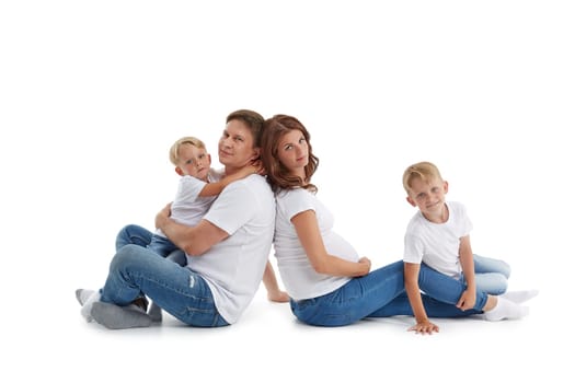 Friendly family. Young pregnant woman and her husband are sitting with backs to each other with children, Isolated on a white background.  Happy parents. Pregnant mother and father with two sons