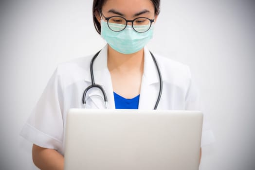 Studio portrait Asian young woman doctor wears glasses and mask to safety Coronavirus looking at the laptop, Physician with stethoscope are working on a computer to stop the epidemic Covid-19 virus