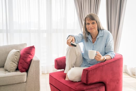 Mature woman in armchair with TV remote and coffee
