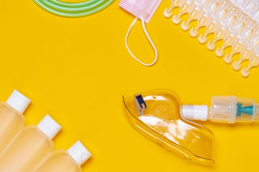 Coronavirus protective measures. Close-up of amedical face mask for treatment of the respiratory tract, ampoules, three bottles of disinfectan and a surgical mask flat layed on a yellow background. Personal protective equipment. Copy space.