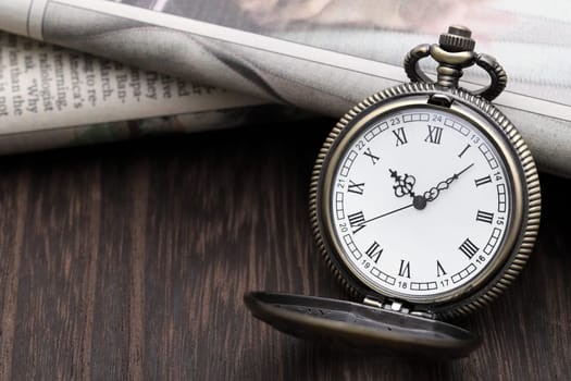 Old pocket watch and newspaper on dark wooden table