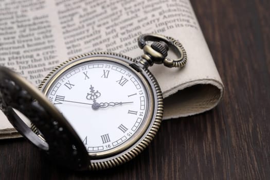 Old pocket watch and newspaper on dark wooden table