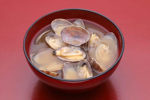 Japanese miso soup with asari clams in a bowl on red wooden table
