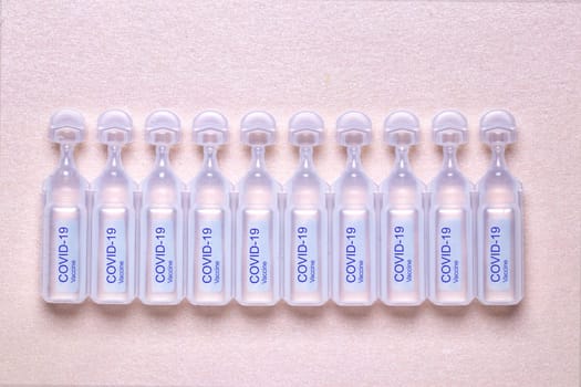 Coronavirus treatment concept. Close-up of ten ampoules with vaccine COVID-19 flat layed on a sparkling light pink paper background. Global pandemic outbreak and healing the deadly coronavirus. Macro photograph.