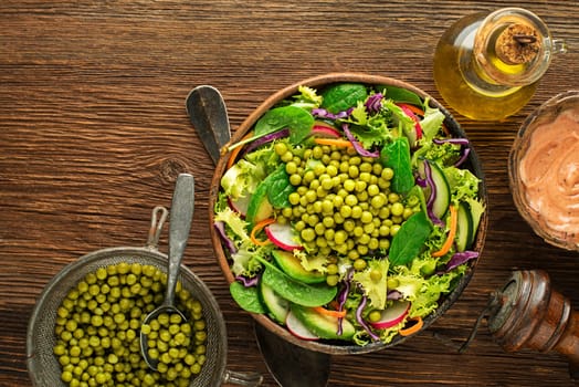 Green lettuce salad meal with fresh vegetables and peas on wooden table background