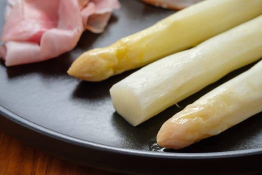 Close-up prepared white asparagus on black plate