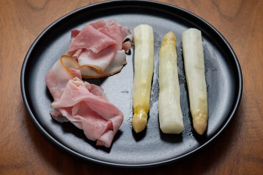 White prepared asparagus with cooked ham on a plate