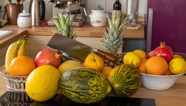 Many varieties of fresh and exotic fruits with a cleaver standing on a cooking island in a domestic kitchen