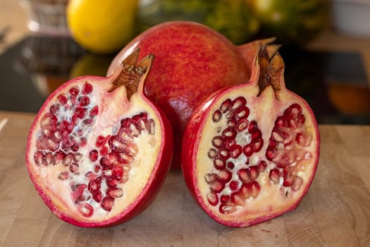 Close up of one whole and two half pomegranates fruits on a wooden cutting board in a domestic kitchen