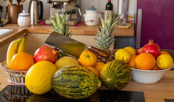 Many varieties of fresh and exotic fruits with a cleaver standing on a cooking island in a domestic kitchen