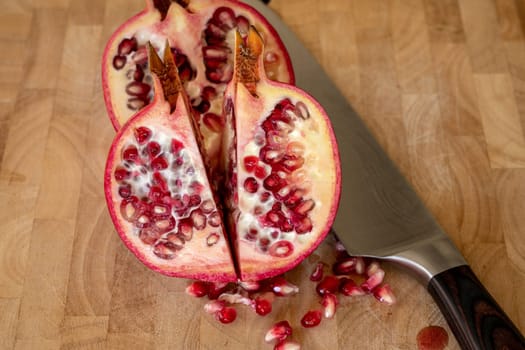 Close up of two half pomegranates fruits and a damascus kitchen knife on a wooden cutting board with pomegranate seeds in the foreground in a domestic kitchen