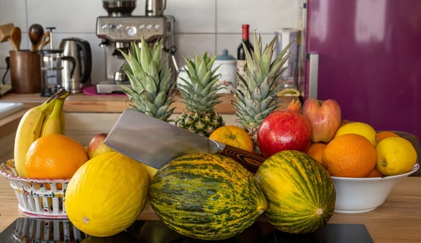 Many varieties of fresh and exotic fruits with a cleaver standing on a cooking island in a domestic kitchen