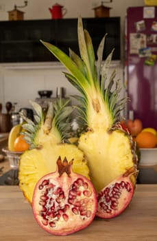 Close-up view of two halve pineapple fruit and a halve Pomegranate fruit on a cutting board in a domestic kitchen with other varieties of fruit in the background