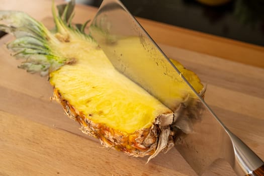 Close-up view of a cleaver in half a pineapple fruit on a cutting board in a domestic kitchen