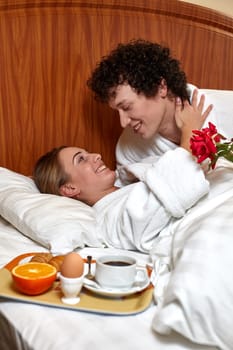 Happy young family  with breakfast lies in the bed at home.