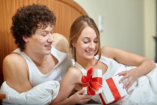 Happy young family with gift box lies in the bed at home. Valentine's Day