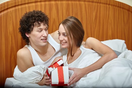 Happy young family with gift box lies in the bed at home. Valentine's Day