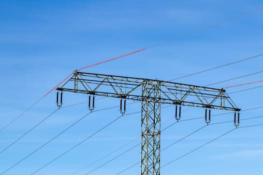 Electric power transmission concept. Selective focus on a electricity supply pylon and the high voltage power lines against a blue cloudy sky.