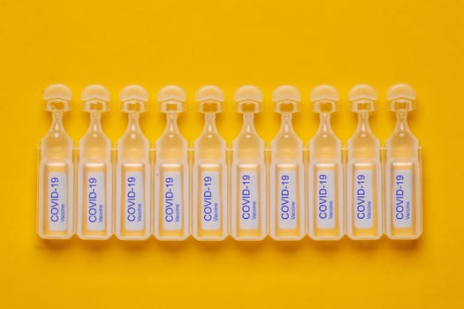 Coronavirus treatment concept. Close-up of ten ampoules with vaccine COVID-19 flat layed on a yellow background. Global pandemic outbreak and healing the deadly coronavirus. Macro photograph.